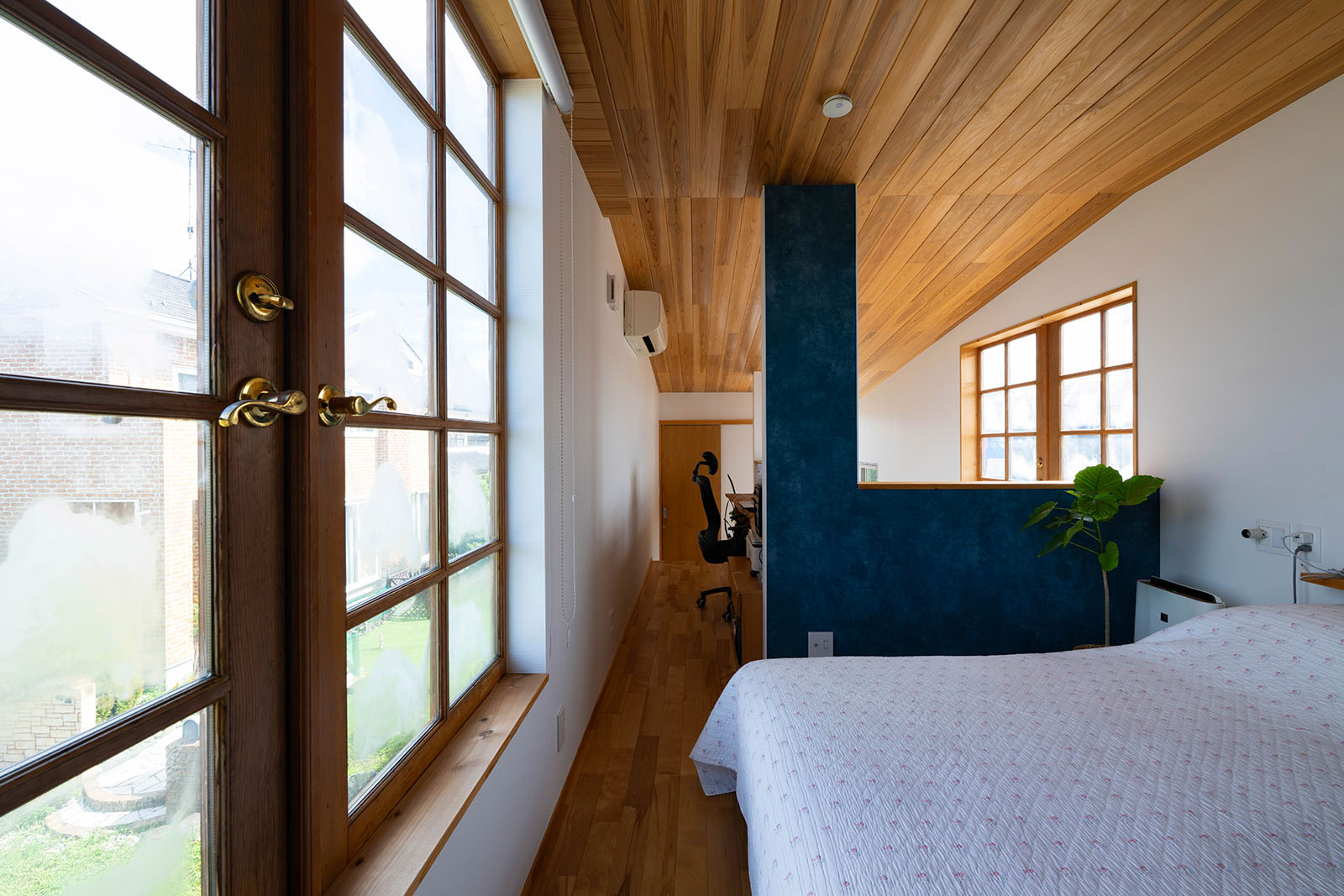 2階はトイレと浴室以外に扉のないワンルームの間取り。北面の窓からの安定した光が寝室を包む。ネイビーブルーのクロスが空間のアクセントに